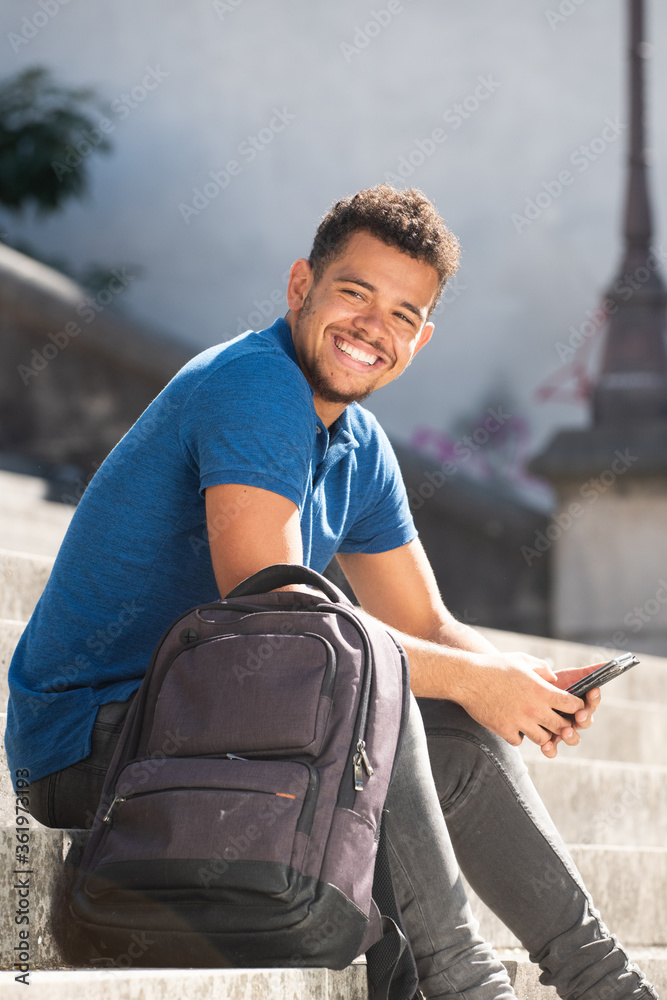 Obraz premium smiling young african american man sitting on steps outside with mobile phone