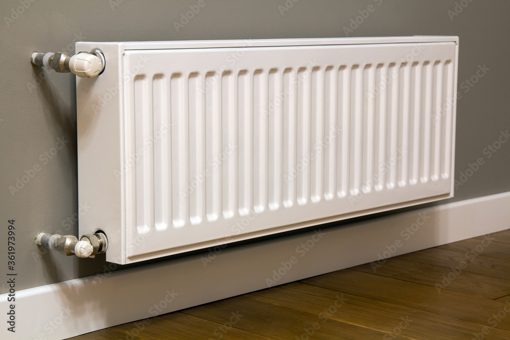 White metal heating radiator mounted on gray wall inside a room. White metal heating radiator mounted on gray wall inside a room.