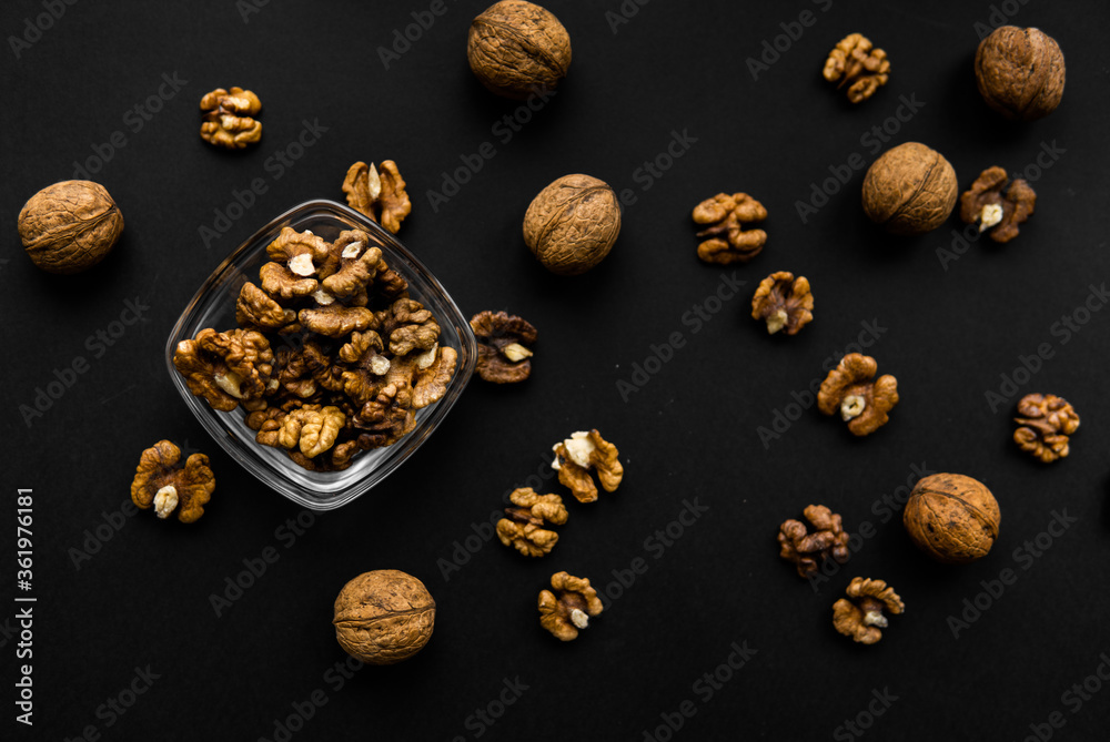 Walnut in a small plate with scattered shelled nuts which standing on a black surface. Walnuts is a healthy vegetarian protein nutritious food. Walnut in a small plate with scattered shelled nuts which standing on a black surface. Walnuts is a healthy vegetarian protein nutritious food.