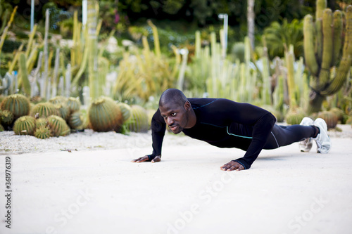 Fit dark skinned man in active clothes doing push-ups exercise outdoors photo