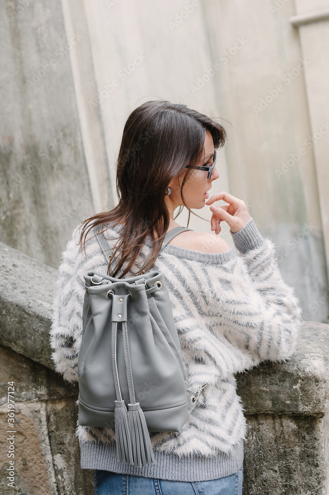 Girl with a gray leather backpack on her shoulders. Back view. Fashion bags. Leather Bucket Bag With Fringe