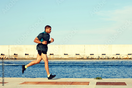 Full length portrait of runner man with muscular body working out near sea with copy space area for your text message or advertising,muscular sportsman engage physical exercises outdoors in summer day