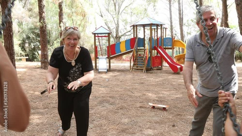 Video in 4k di nonni bianchi che spingo nell'altalena le due nipoti di origine sud americana nel parco giochi di una pineta photo