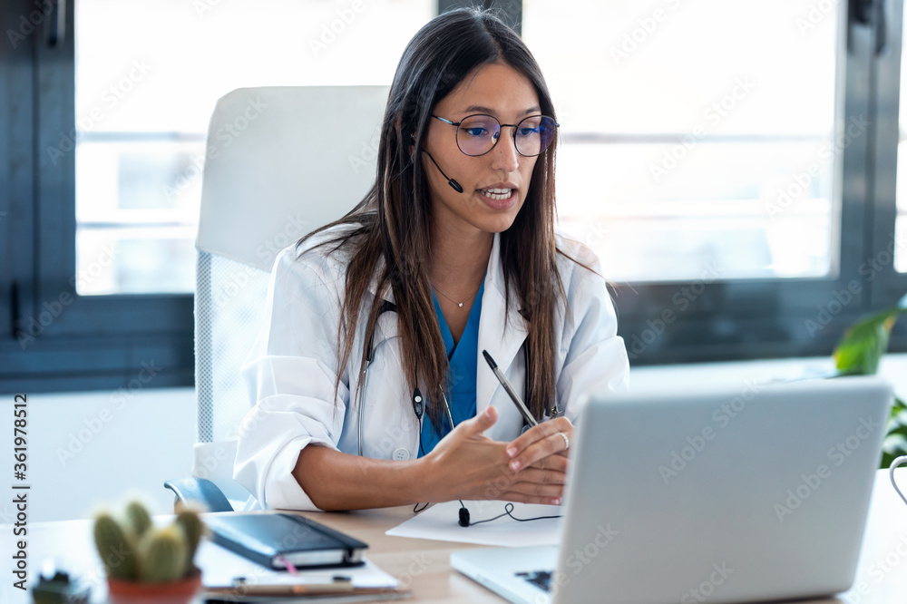 Female doctor talking with colleagues through a video call with a laptop in the consultation.