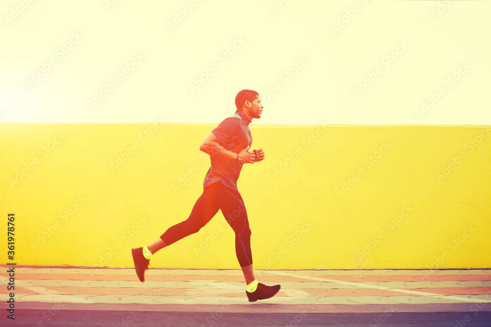 Obraz premium Full length portrait of afro american runner with muscular body in tracksuit jogging against yellow wall with copy space area for your text message or content, young male jogger working out outdoors