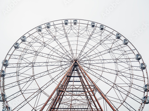 Photo From the bottom up of a tall modern Ferris wheel with enclosed booths against a cloudy sky.