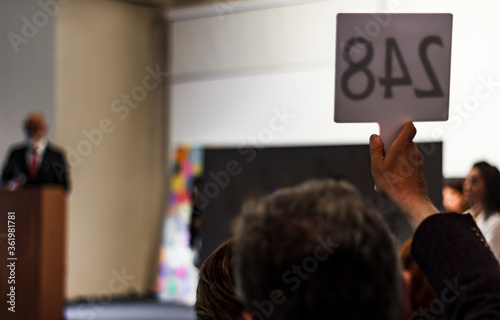 Ongoing auction session. a buyer raises his number sign to buy a painting