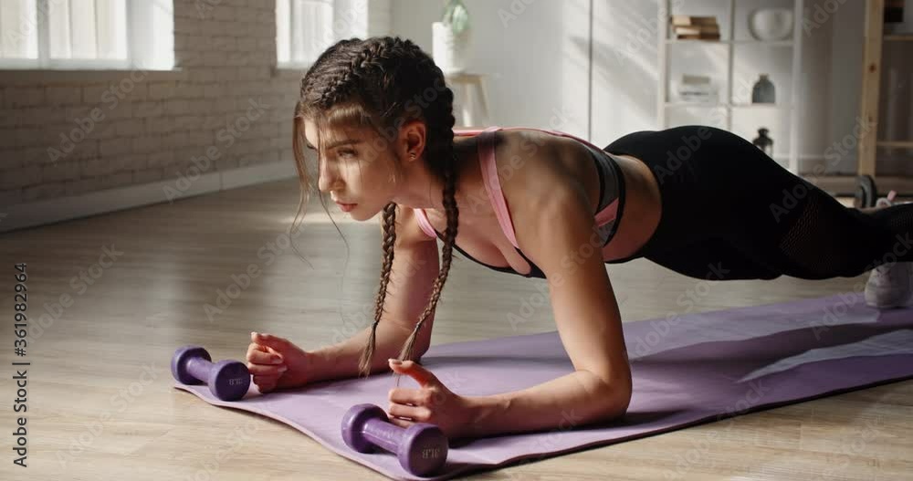 Young fit attractive caucasian girl doing a plank exercise. Determined female athlete does sports at home, training with cross fit system - healthy lifestyle concept 4k footage