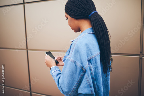 Fotografie Back view of afro american stylish young woman with pigtails dialing phone number on telephone standing on promotional background