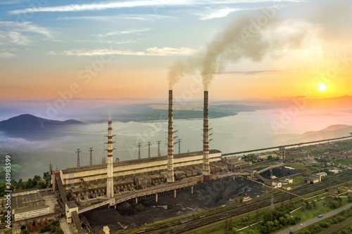 High power plant pipes with thick dirty smoke with wide valley with white fog and big lake between green mountains.