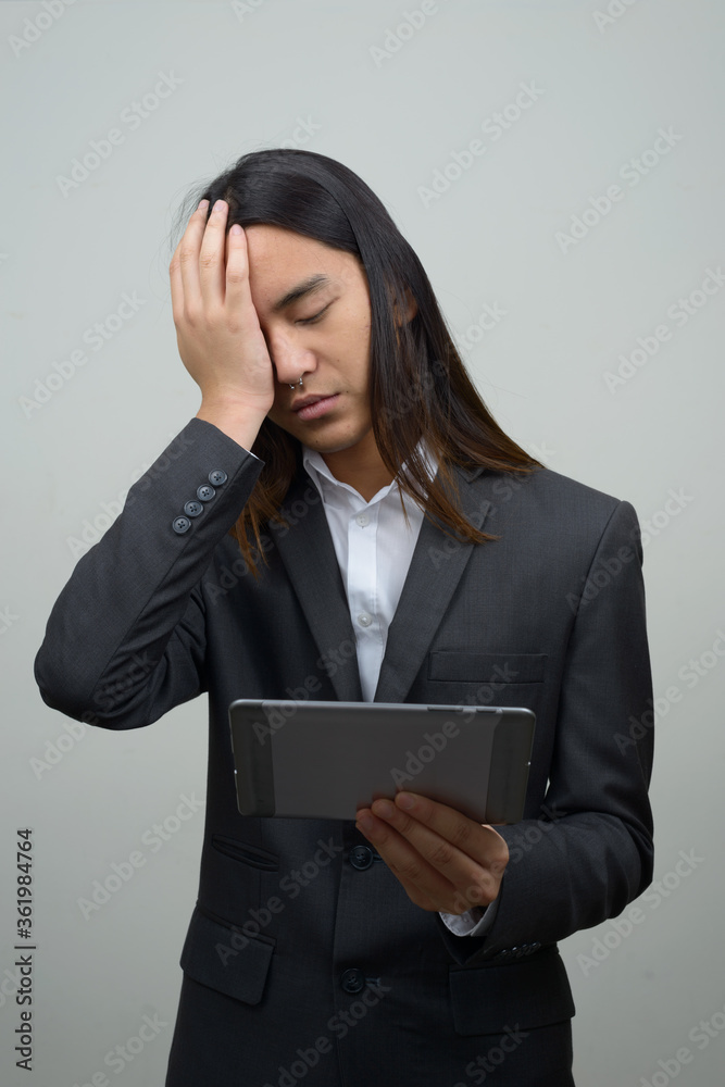 Stressed young Asian businessman with long hair getting bad news while using digital tablet Stressed young Asian businessman with long hair getting bad news while using digital tablet