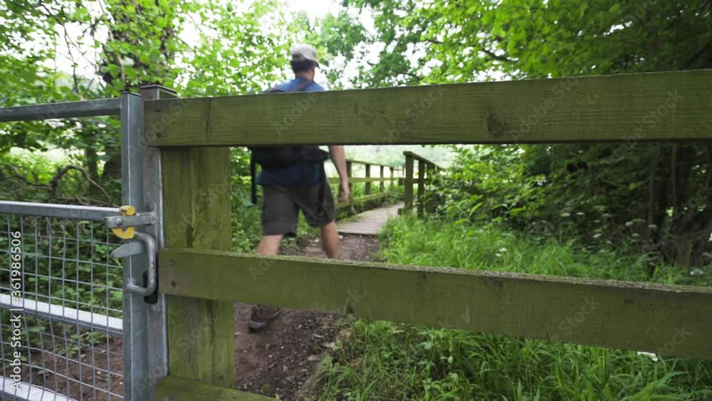 A man walking through a countryside gate and over a wooden bridge A man walking through a countryside gate and over a wooden bridge