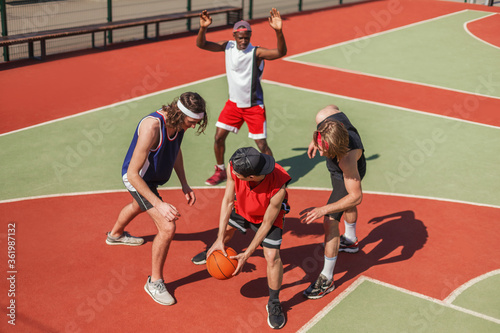 Young multiethnic sportsmen playing basketball game at outdoor playground