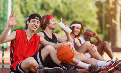Asian player and his multinational team having rest on basketball arena outdoors, empty space