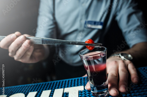 The barman decorates the alcoholic cocktail with berry using the pliers. Close-up