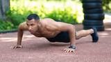 Shirtless muscular black guy performing push ups on jogging track at city park