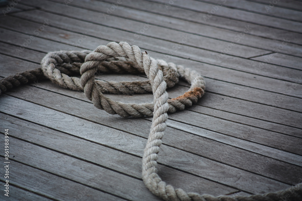 Obraz premium Thick rope coiled on a wooden floor.