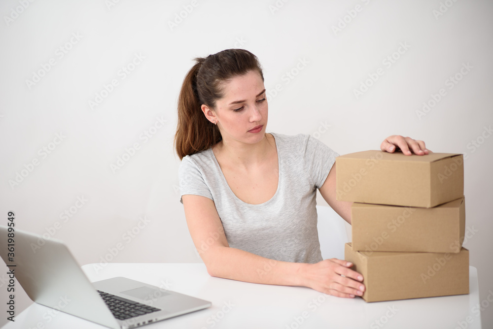 Girl with ponytails, a gray T-shirt sits at a laptop and looks at a stack of cardboard boxes. Online delivery service Girl with ponytails, a gray T-shirt sits at a laptop and looks at a stack of cardboard boxes. Online delivery service