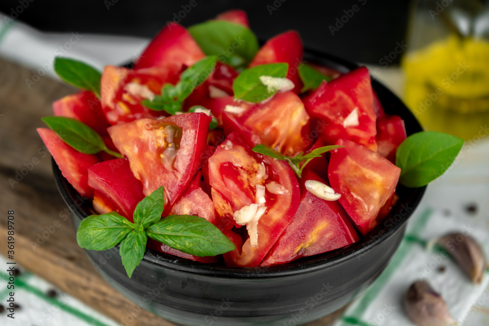 fresh ripe tomato slices and green basil salad in a black bowl on a wooden cutting board fresh ripe tomato slices and green basil salad in a black bowl on a wooden cutting board