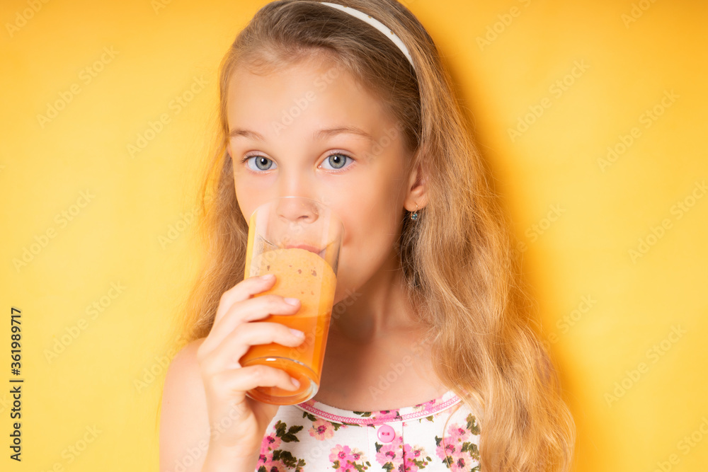 Cute little girl with flying blond hair enjoys carrot juice with great pleasure drinking. Close up shot isolated on yellow, copy space. Childhood, healthy nutrition, vitamins, summertime Cute little girl with flying blond hair enjoys carrot juice with great pleasure drinking. Close up shot isolated on yellow, copy space. Childhood, healthy nutrition, vitamins, summertime