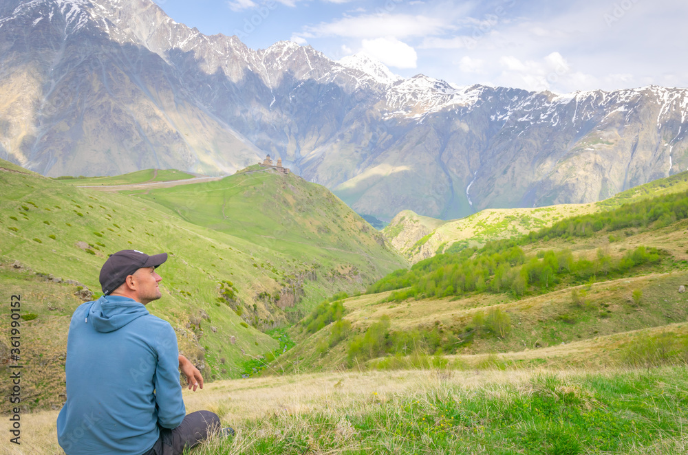 Smilling male person sits and enjoys the views of Kazbegi nationa park green nature and mountains in the background. Tourism in Georgia.2020