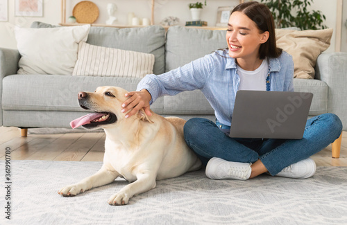 Billede på lærred Young woman at home with laptop and happy dog