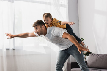 handsome father piggybacking happy son imitating flying with outstretched hands