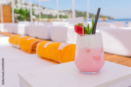 strawberry cocktail in front of a white background. cold pink cocktail with ice on the beach club in hot summer day. cocktail image with foam on the background with sun beds and towels