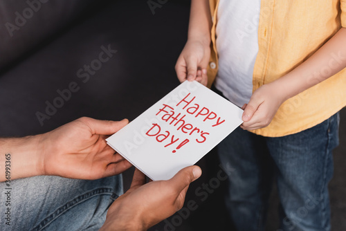 cropped view of boy presenting happy fathers day greeting card to father photo