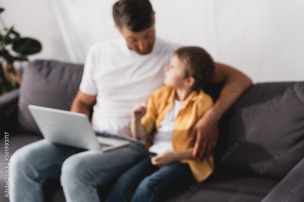 selective focus of father and son sitting on sofa, talking and using laptop selective focus of father and son sitting on sofa, talking and using laptop