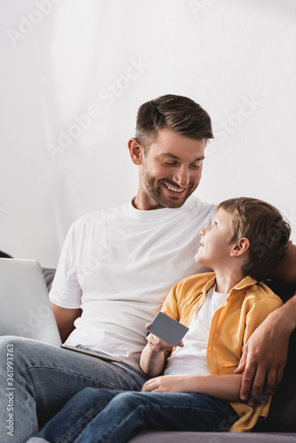 happy father with laptop looking at smiling son holding credit card