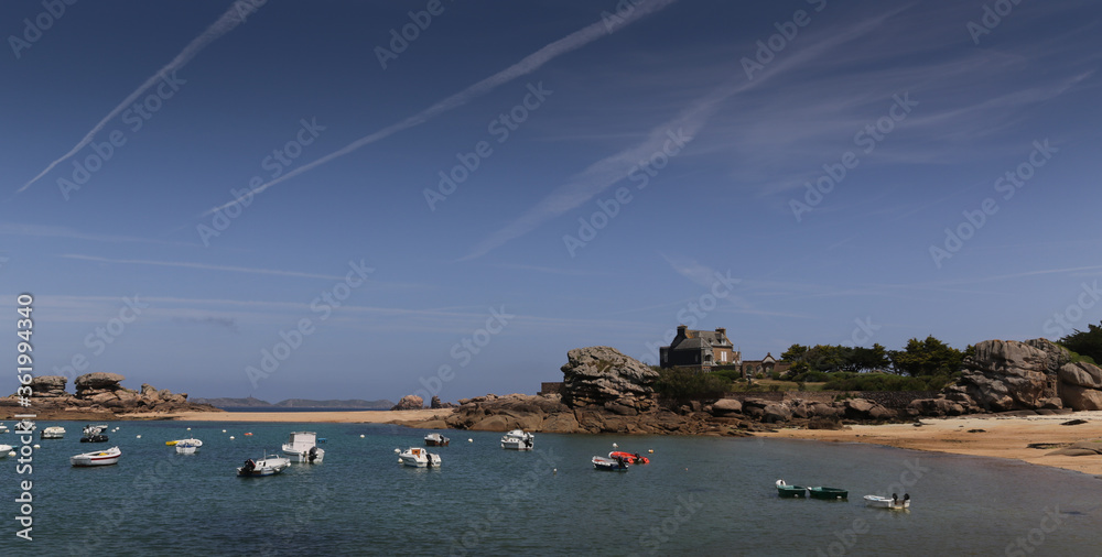 Boats on a sunny day in the bay of the sandy beach of Coz-Porz with large granite boulders on the English Channel in Tregastel (Brittany, France)