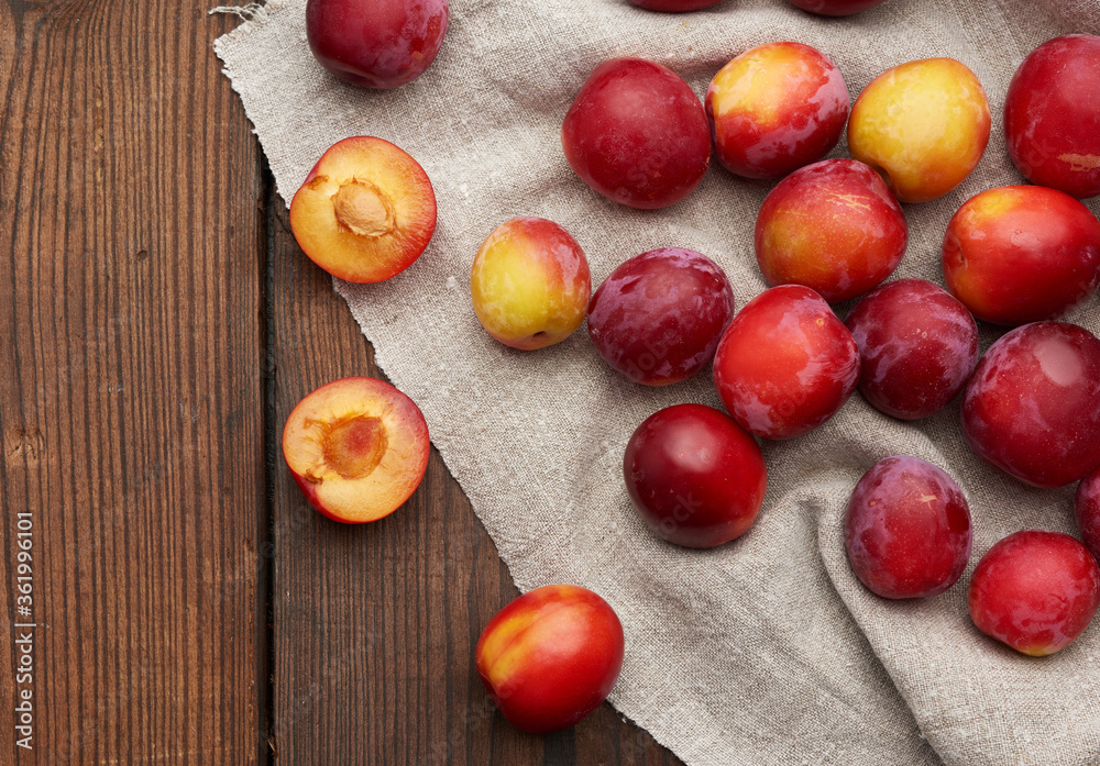 ripe red plums on a gray linen towel, brown wooden table