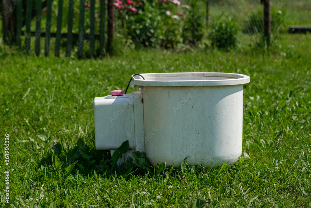 An old and idle white small washing machine stands on a lawn with green grass in the garden. An old and idle white small washing machine stands on a lawn with green grass in the garden.