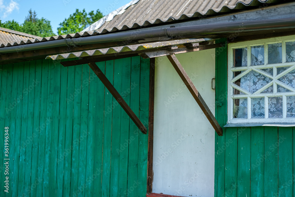 Visor (small roof) above the stairs at the entrance to the green country house with white windows and a door.