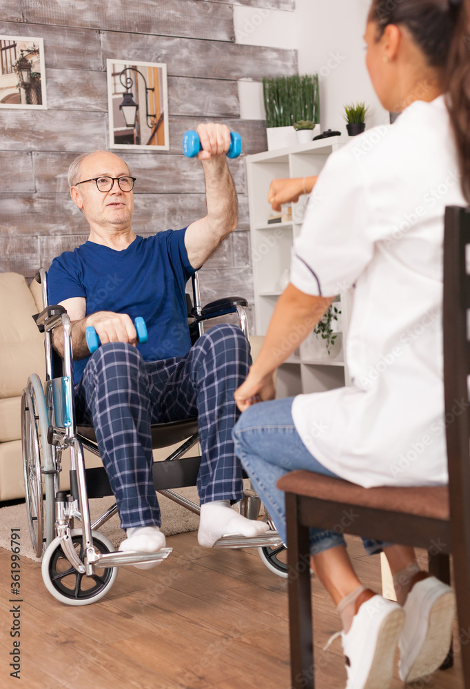 Grandfather in wheelchair doing sport assisted by nurse. Disabled handicapped old person with social worker in recovery support therapy physiotherapy healthcare system nursing retirement home Grandfather in wheelchair doing sport assisted by nurse. Disabled handicapped old person with social worker in recovery support therapy physiotherapy healthcare system nursing retirement home