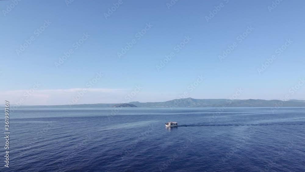 Drone flying shot following fishing boat at calm sea in Greece. Aerial top view of caique sailing at Kassandra Chalkidiki peninsula with background Sithonia view. Drone flying shot following fishing boat at calm sea in Greece. Aerial top view of caique sailing at Kassandra Chalkidiki peninsula with background Sithonia view.