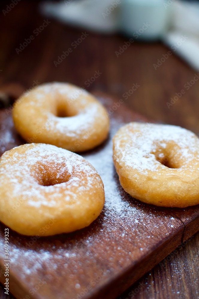 Three powdered sugar donuts on rustic table for snack food or breakfast.