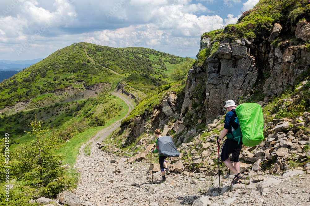 A pair of hikers with backpacks descend the mountain trail in the direction of the next peak