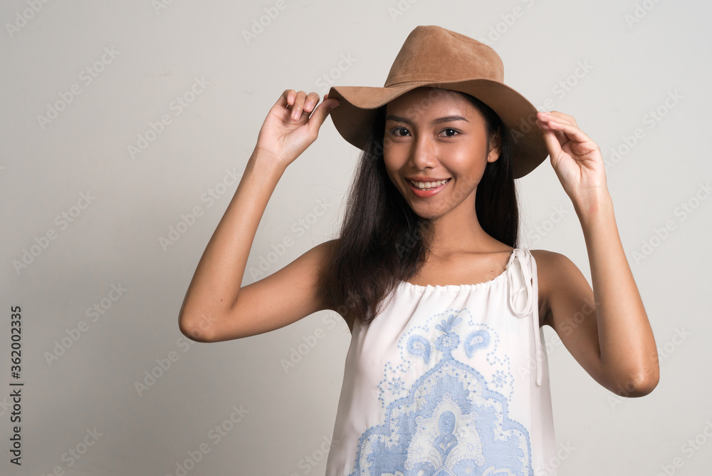Happy young beautiful Asian teenage girl as tourist holding hat Happy young beautiful Asian teenage girl as tourist holding hat