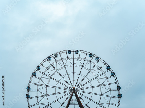 High modern ferris wheel with closed booths on a background of blue sky