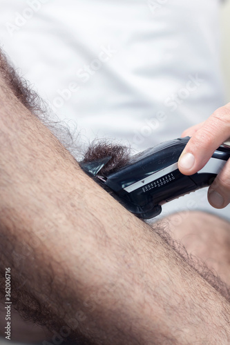Mężczyzna trzyma w dłoni maszynkę do strzyżenia i obcina włosy na łydce. photo