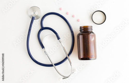 Pills, medical bottle and stethoscope on a white table.