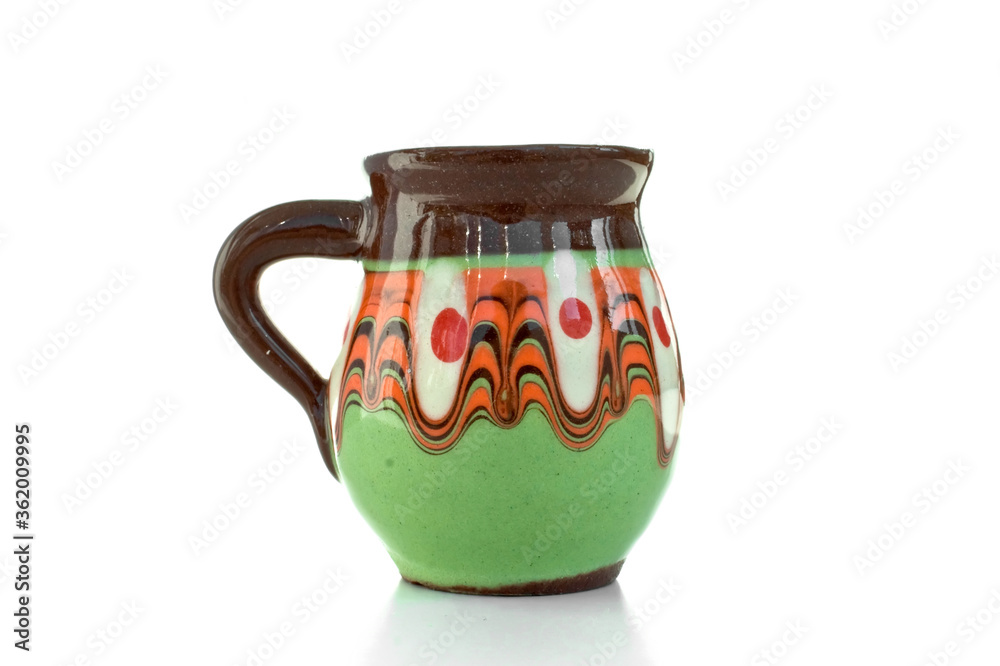 Close up cute pot with colorful painting, green orange brown clay jar with handle, traditional bulgarian decoration souvenir. Pottery, earthenware, classic hand crafted activity. White background.  