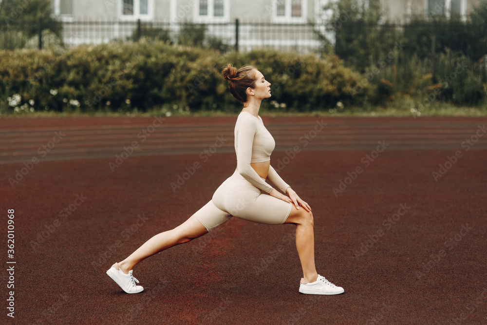 A sporty woman trains and exercises at a fitness stadium. Warm-up in the open air, stretching.