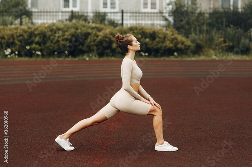 A sporty woman trains and exercises at a fitness stadium. Warm-up in the open air, stretching.