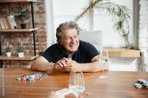 Exciting. Happy mature man playing cards and drinking wine with friends. Looks delighted, excited. Caucasian man gambling at home. Sincere emotions, wellbeing, facial expression concept. Good old age.