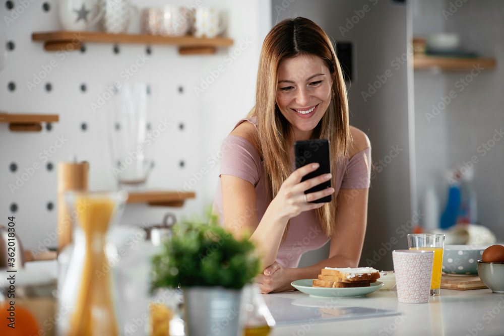 Young woman in the kitchen. Beautiful woman drinking juice and using  the phone.	
