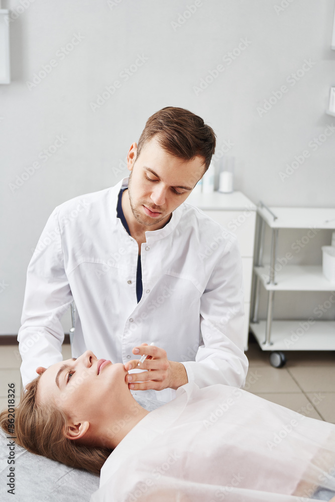 Fototapeta premium Cosmetologist doctor makes markings on the face of young woman patient, preparing for procedure of botulinum therapy for wrinkles in white beauty parlor