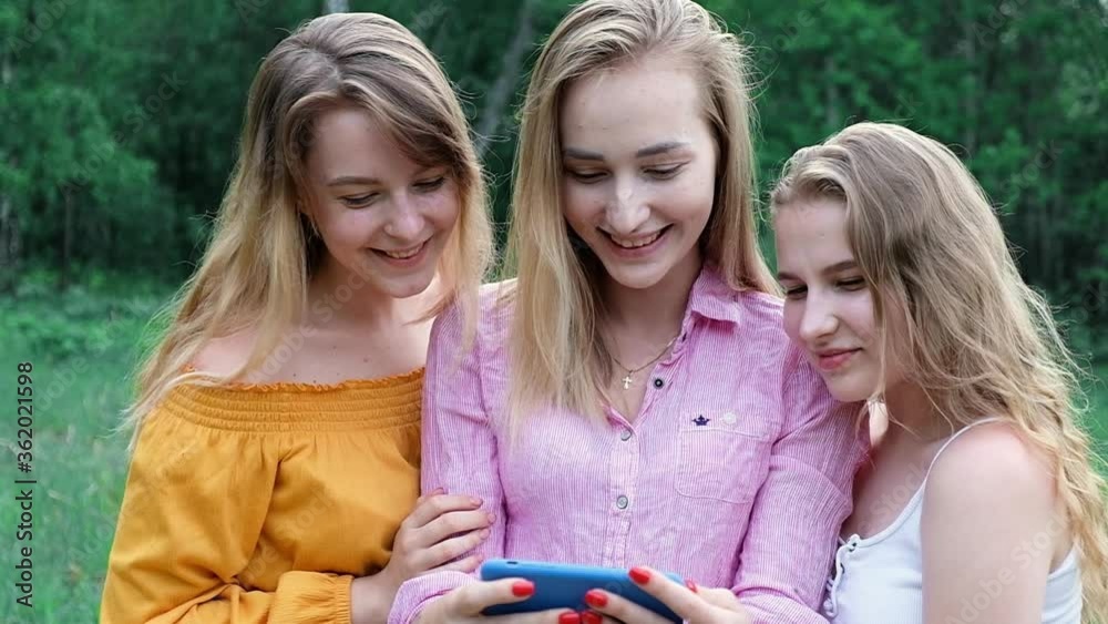 Friends in Park on picnic look at smartphone scroll through photo and enjoy vacation in nature in forest. Girls laugh and have fun on a weekend picnic with the phone. Online vacation outside the home Friends in Park on picnic look at smartphone scroll through photo and enjoy vacation in nature in forest. Girls laugh and have fun on a weekend picnic with the phone. Online vacation outside the home